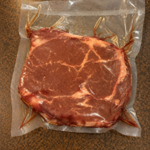 Raw steak in sealed plastic wrap