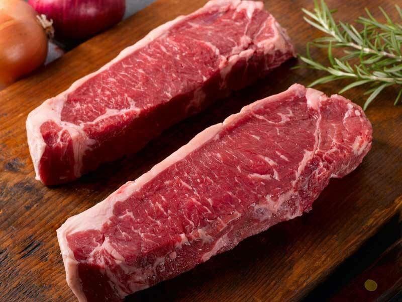 Two raw beef steaks on wooden cutting board