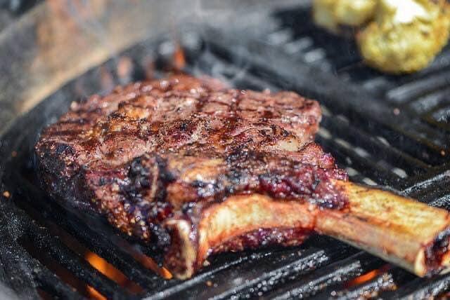 Bone-in ribeye steak grilling on barbecue