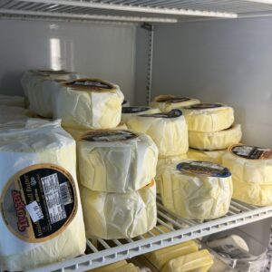 Wrapped cheese wheels stacked on refrigerator shelves