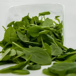 Fresh baby spinach spilling from plastic container