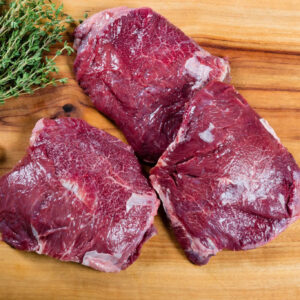 Three raw beef steaks on wooden cutting board