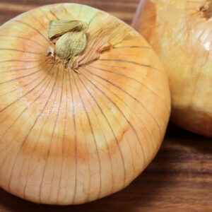 Two yellow onions on wooden cutting board